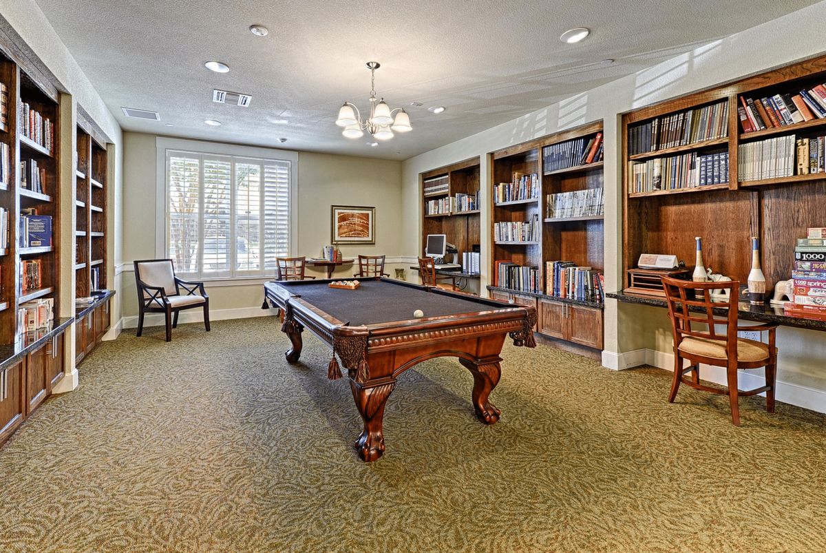 A cozy billiard room with bookshelves, featuring a classic pool table and elegant decor.