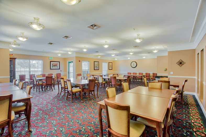 A spacious dining area with multiple tables and chairs, featuring a carpeted floor and overhead lighting.