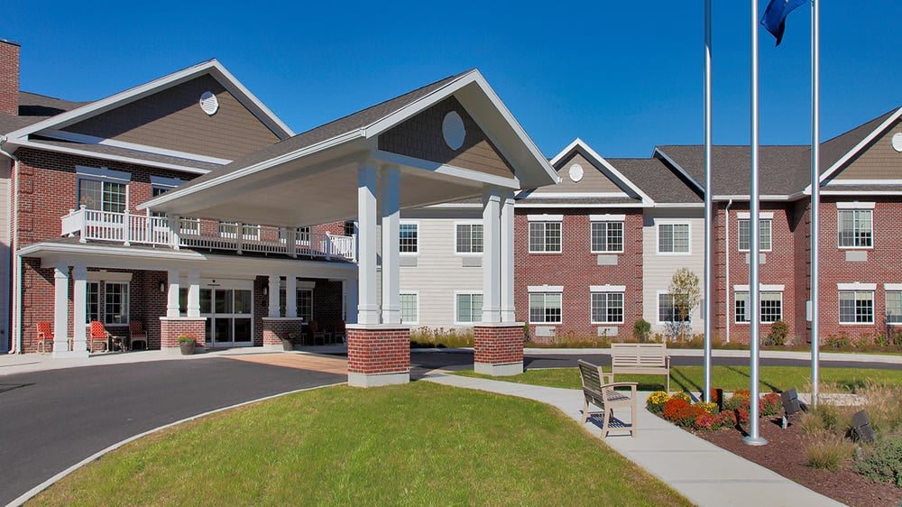 A modern senior living facility with a landscaped entrance and clear blue skies.