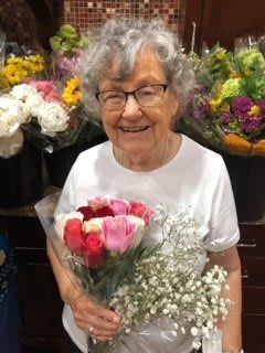 An elderly woman smiling while holding a bouquet of colorful flowers.
