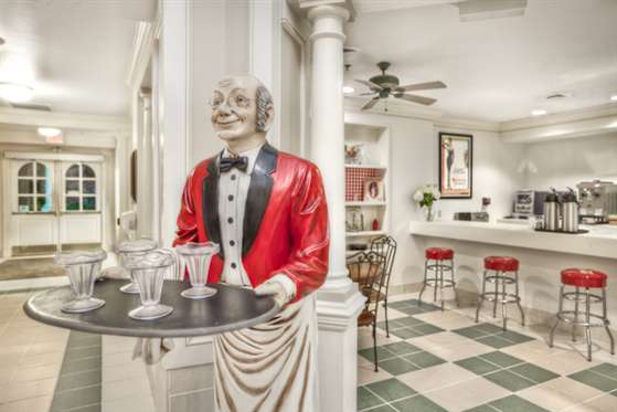 A statue of a waiter in a red jacket holding a tray, set in a stylish kitchen bar area.