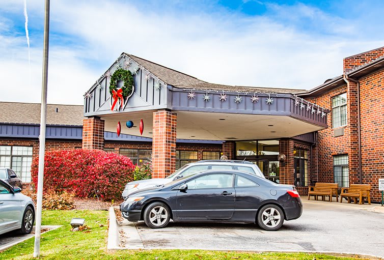 A building entrance decorated with a holiday wreath, featuring cars parked in front.