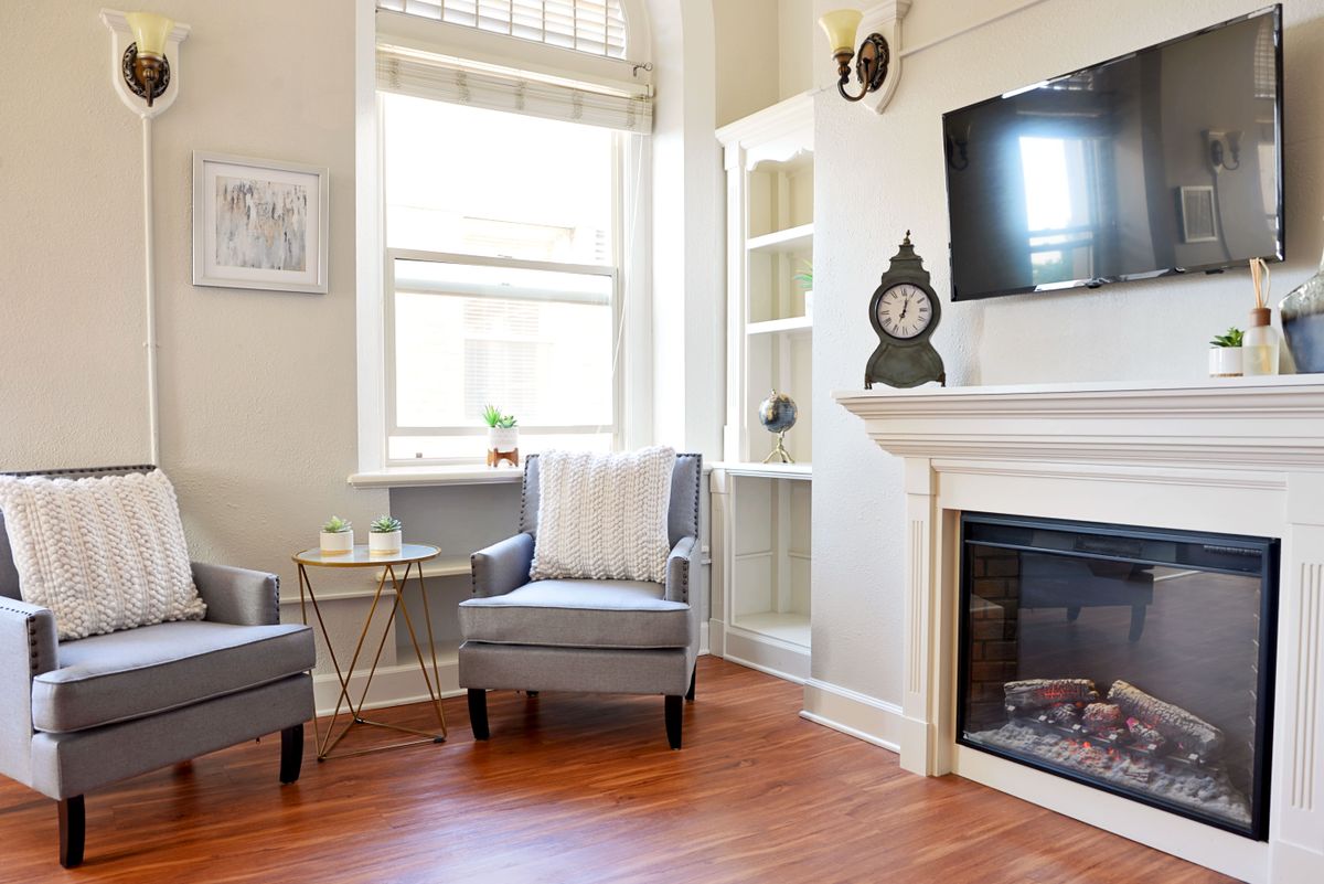 A cozy living room with a fireplace, two gray chairs, and a mounted television.