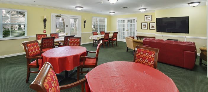 A cozy dining area with multiple tables covered in red tablecloths, arranged in a well-lit community space.