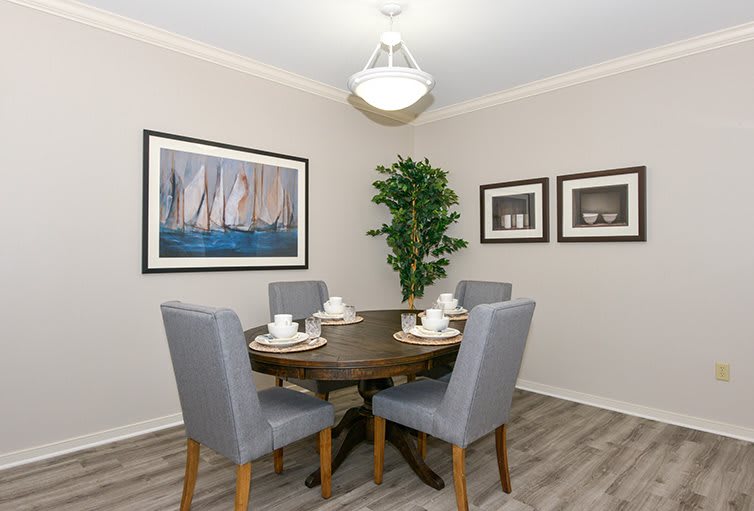 A cozy dining room with a round table set for four, featuring modern art and a decorative indoor plant.