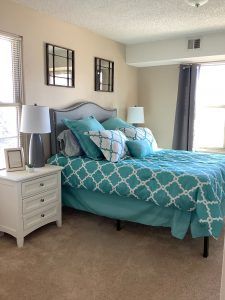 A cozy bedroom with a neatly made bed featuring teal bedding and multiple pillows, accompanied by two nightstands with lamps.
