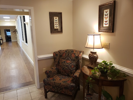 A cozy waiting area featuring a floral patterned chair, decorative lamp, and wall art.