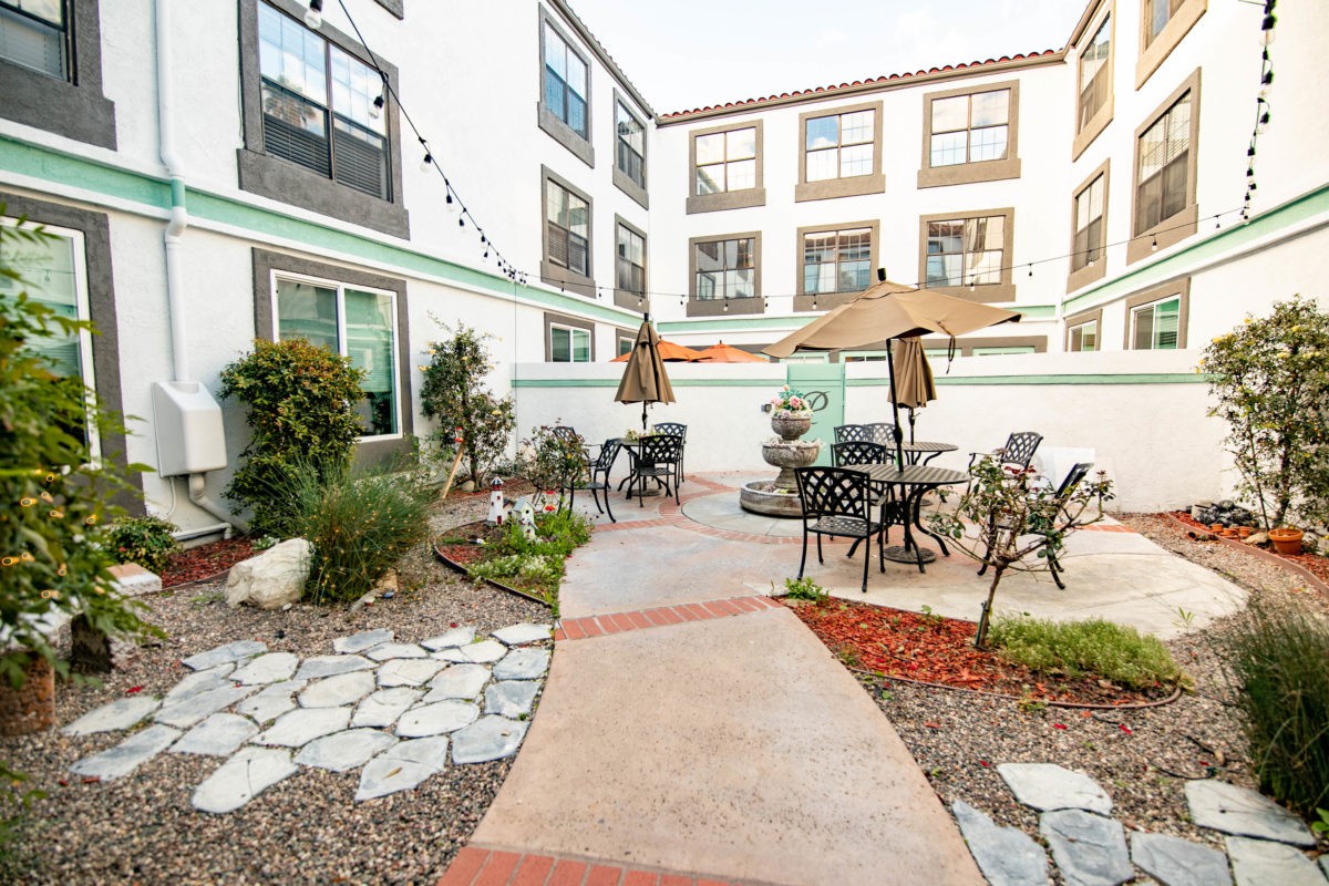 A cozy courtyard with outdoor seating and umbrellas, surrounded by an apartment building.