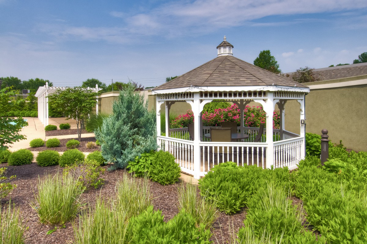 A charming gazebo surrounded by a beautifully landscaped garden under a clear blue sky.