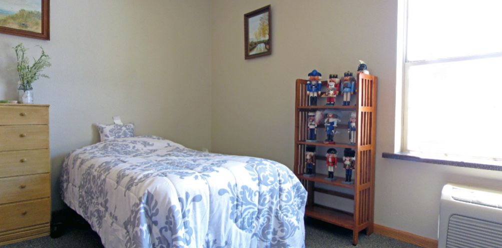 A cozy bedroom featuring a neatly made bed, a wooden shelf displaying toys, and framed artwork on the wall.