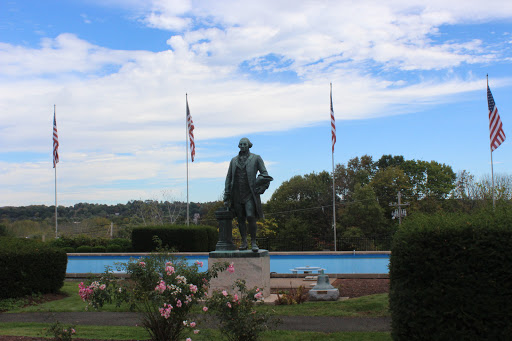 A statue standing proudly in a park, framed by flags and under a beautiful blue sky.
