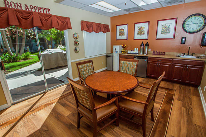A cozy dining area with a round table, surrounded by chairs and a coffee station in a brightly lit room.