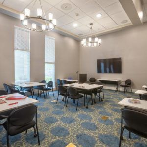 A spacious and well-lit conference room equipped with tables, chairs, and a projector screen.