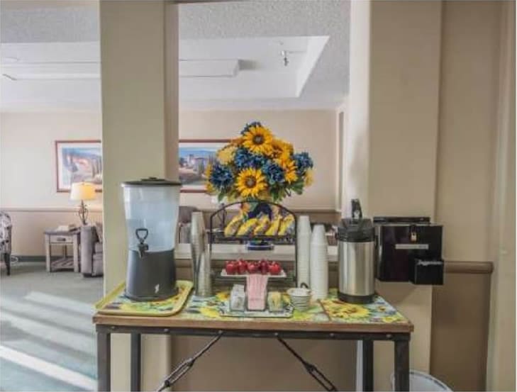 A breakfast setup featuring a coffee station, water dispenser, and pastries, decorated with vibrant sunflowers.