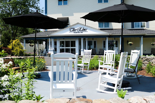 A cozy outdoor seating area featuring white rocking chairs and umbrellas, perfect for relaxation at a restaurant.