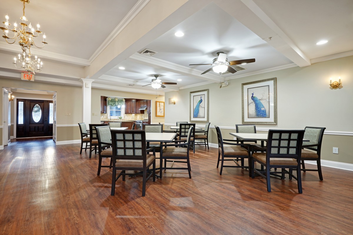 A spacious dining area with several tables and chairs, featuring wooden flooring, ceiling fans, and framed artwork on the walls.