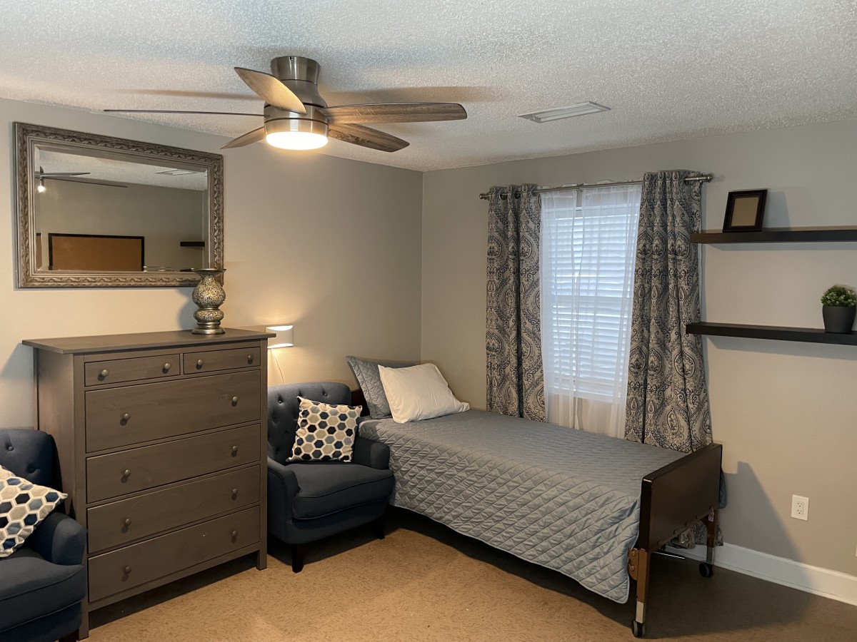 A cozy bedroom with a single bed, armchair, dresser, and desk.