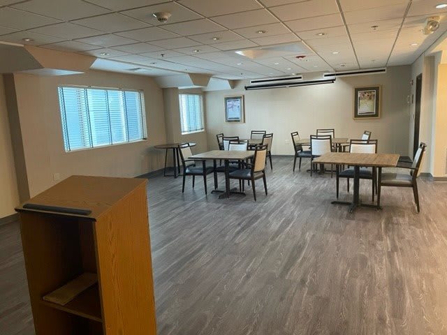 An empty dining area with several tables and chairs, well-lit by windows.