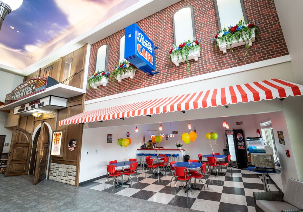 A vibrant diner with red chairs and a checkered floor, featuring a striped awning and flower boxes.