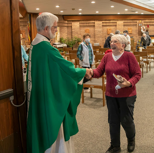 A priest greets an elderly woman after a church service, highlighting community and fellowship.