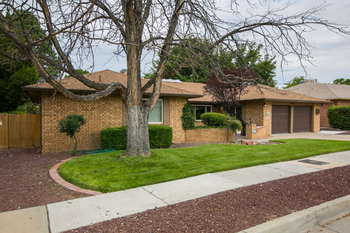 A single-story brick house with a neatly maintained yard and tree, bordered by a sidewalk.