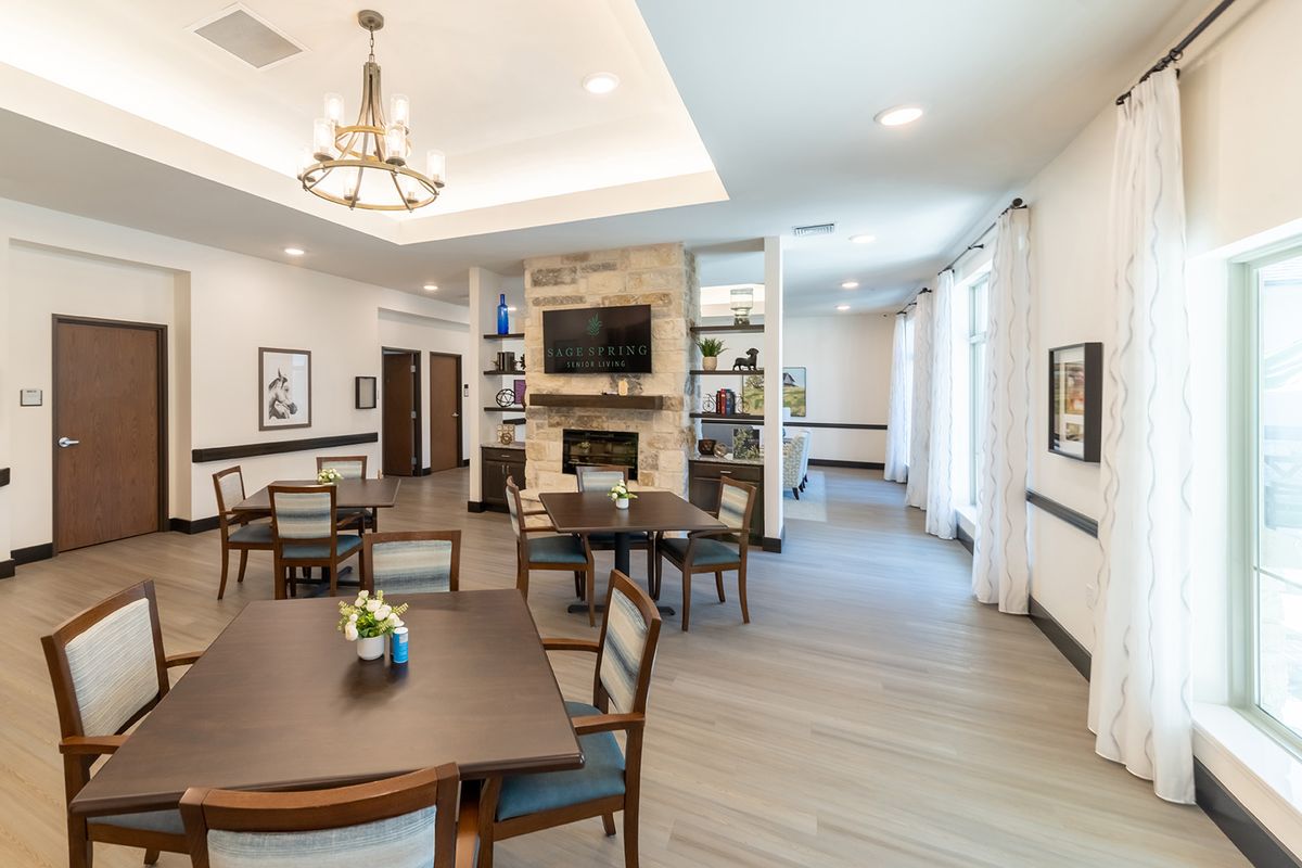 A well-lit dining area featuring multiple tables and chairs, a fireplace with a mounted TV, and wood flooring.