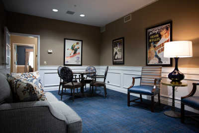A cozy sitting room with a table and chairs, featuring wall posters and carpeted flooring.