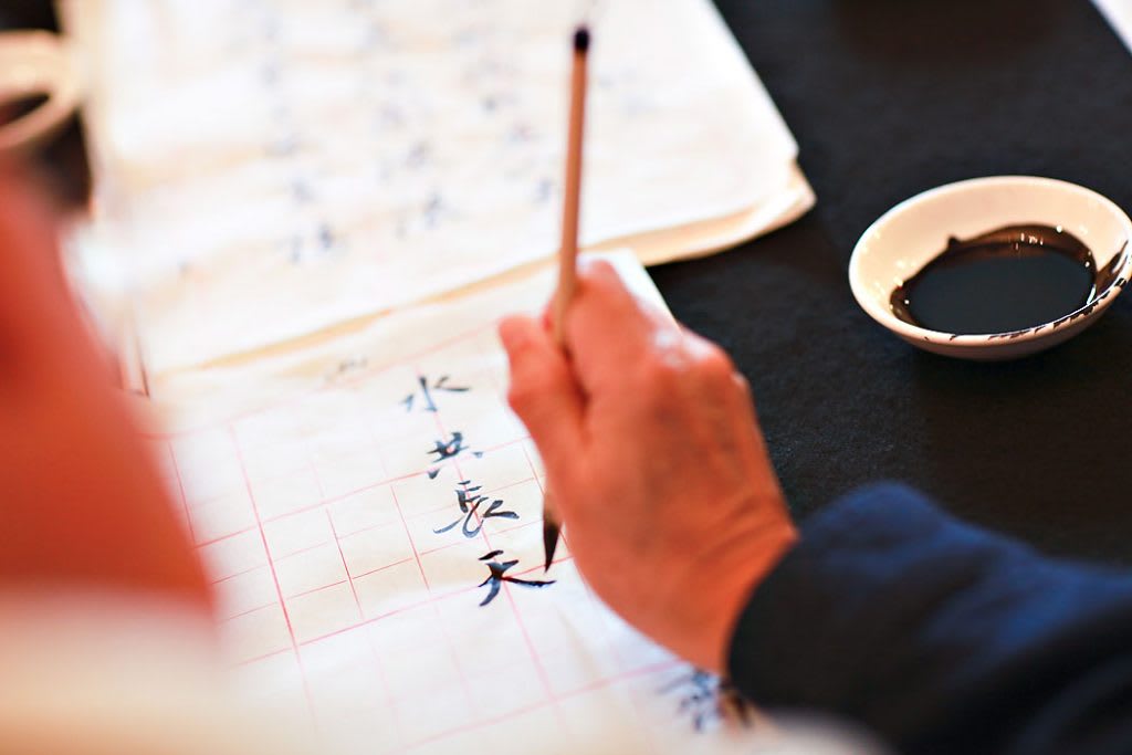 A person practicing calligraphy with a brush pen on paper.