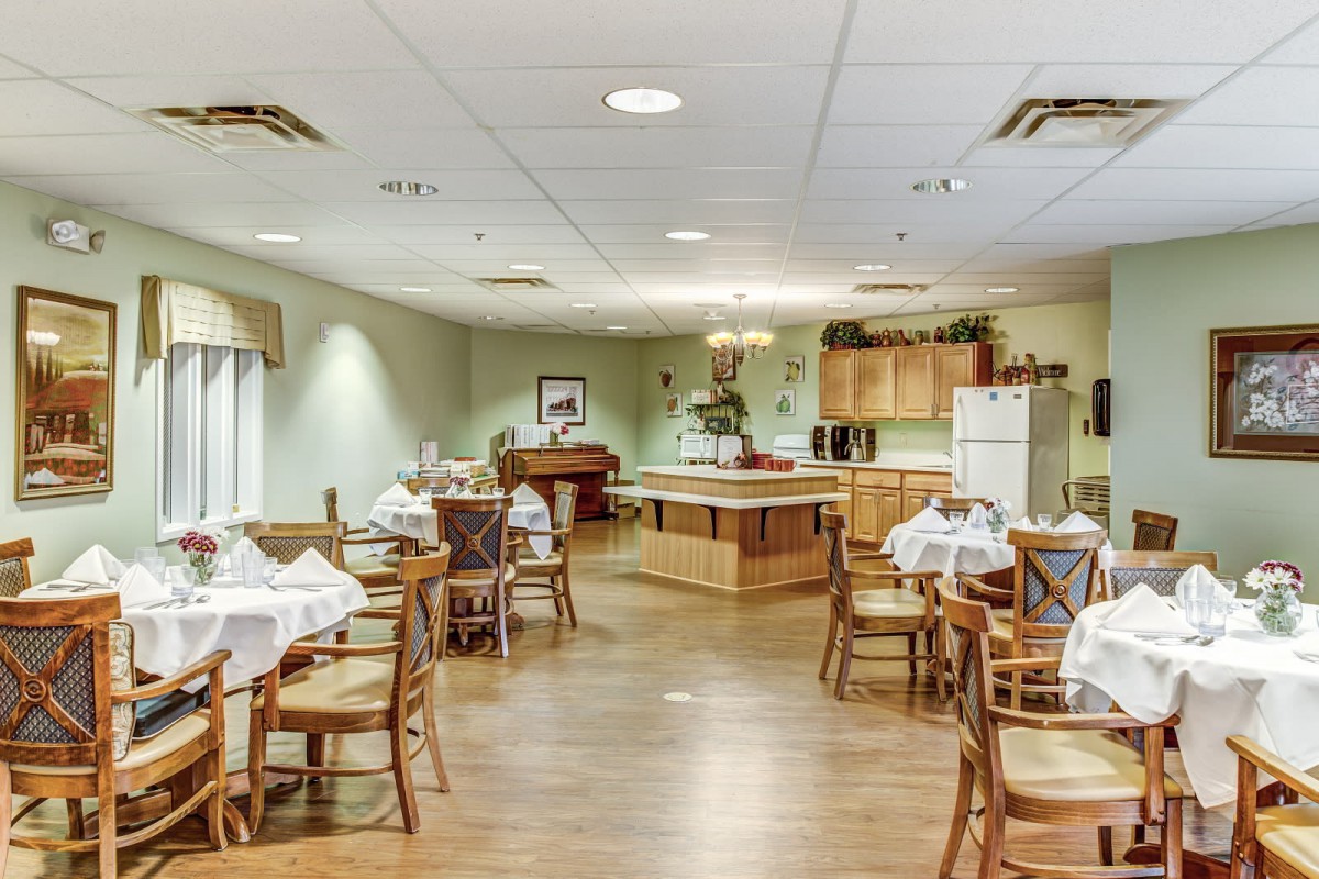 A well-organized dining room with neatly arranged tables and chairs, featuring a kitchen area in the background.