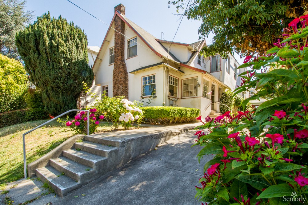 A charming residential house with a colorful garden and a sloped driveway.