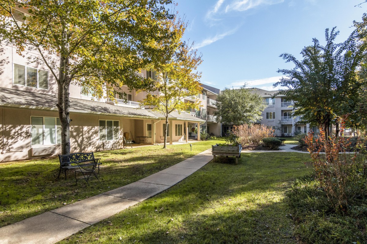 A scenic view of a residential apartment complex with lush green lawns and trees on a sunny day.