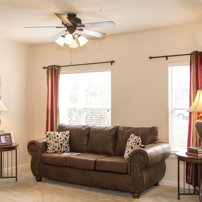 A cozy living room featuring a brown sofa, ceiling fan, and warm lighting.