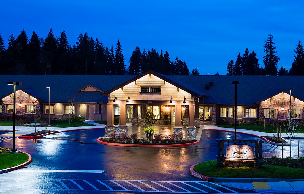 A well-lit building entrance at night, surrounded by a parking area and trees.