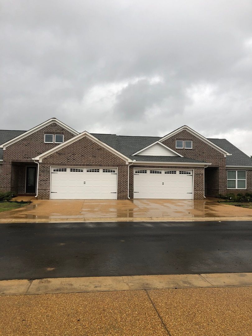 A duplex with brick exterior and two garage doors on an overcast day.