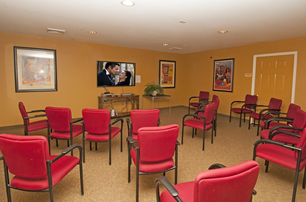 A cozy meeting room with red chairs facing a television and walls adorned with artwork.