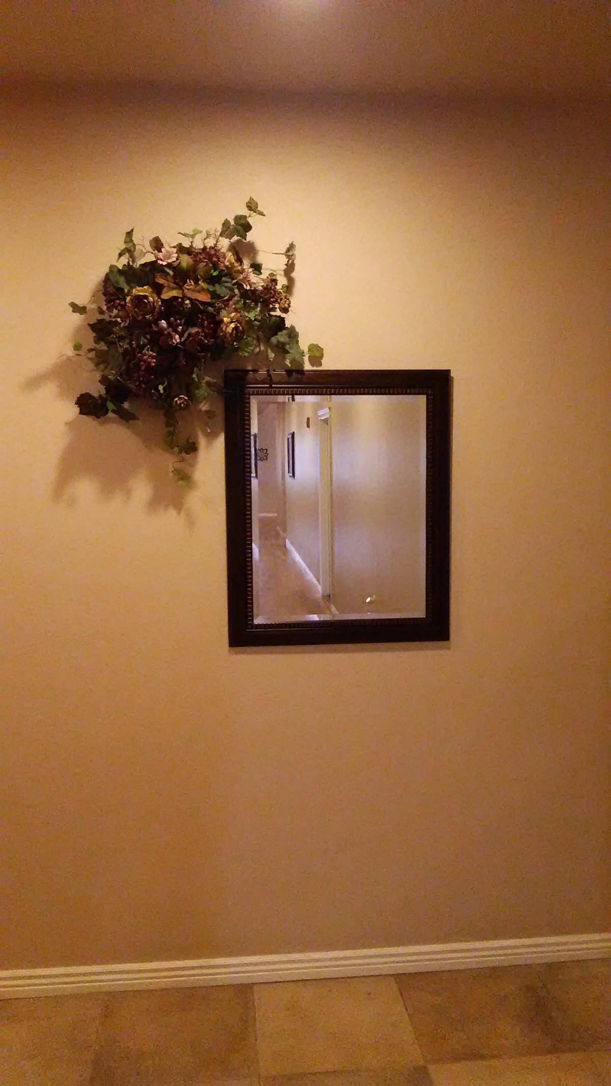 A wall-mounted mirror with a decorative flower arrangement above it.
