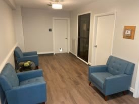 A simple waiting room with blue chairs and wooden flooring.