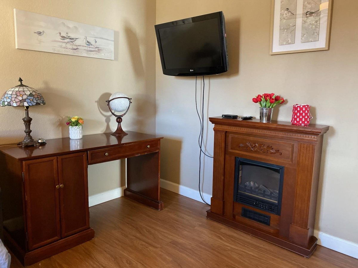 A cozy living room corner with a wooden desk, electric fireplace, and wall-mounted television.