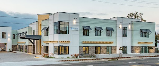 A modern commercial building featuring a blend of green and beige exterior with multiple windows.