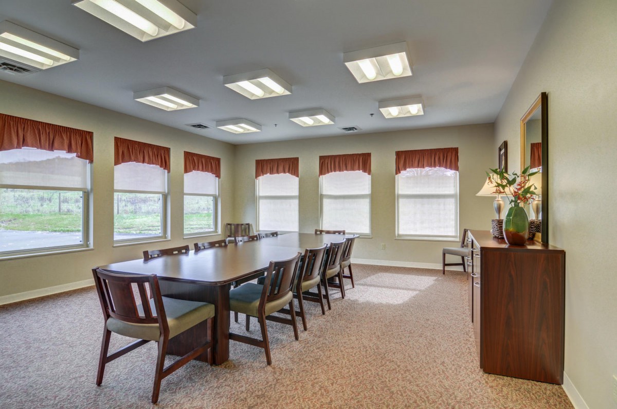A well-lit conference room with a large meeting table surrounded by chairs and windows.
