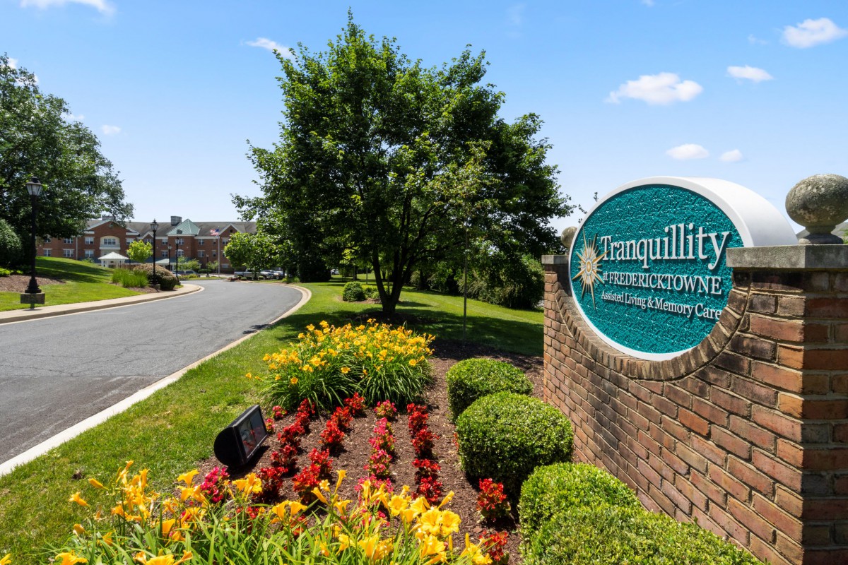 A landscaped entrance with a sign and vibrant flowers alongside a road.