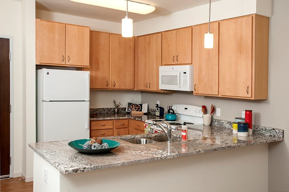 A modern kitchen with wooden cabinets and granite countertops, featuring appliances like a microwave and refrigerator.