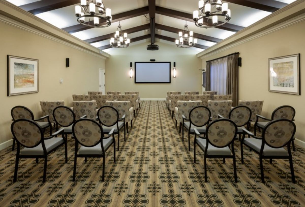 A well-equipped conference room featuring rows of chairs facing a large screen, with chandeliers overhead and a patterned carpet.