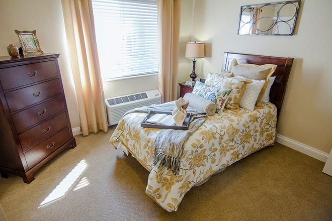 A cozy bedroom with a neatly made bed, soft lighting, and a window allowing natural light.