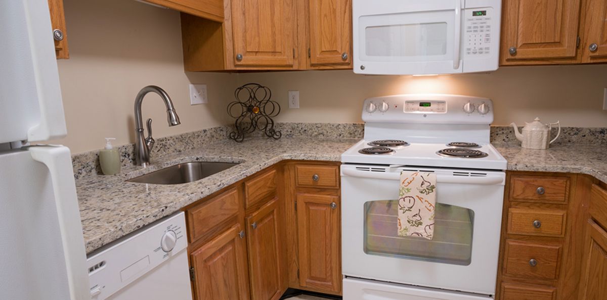 A modern kitchen setup featuring wooden cabinets, a granite countertop, and standard appliances including an oven and microwave.