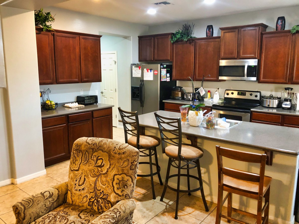 A modern kitchen with wooden cabinets, a countertop with bar stools, and various appliances.