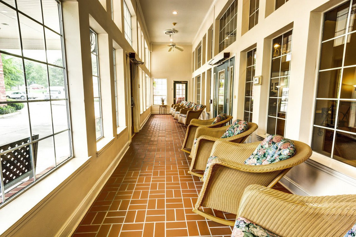 A sunlit hallway featuring wicker chairs and large windows with a brick floor.