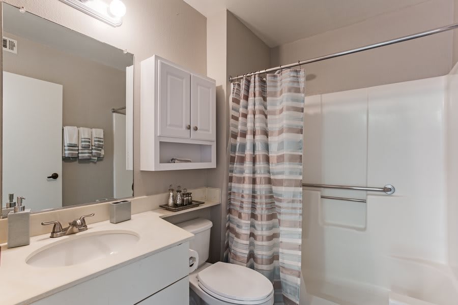 A modern bathroom featuring a sink, toilet, and shower with a striped curtain.