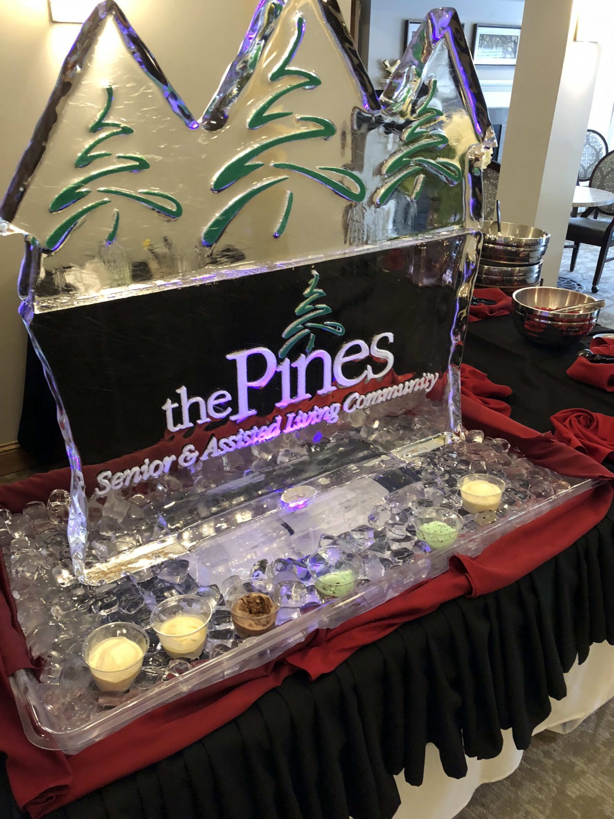 An intricately designed ice sculpture display featuring candles, promoting The Pines Senior & Assisted Living Community.