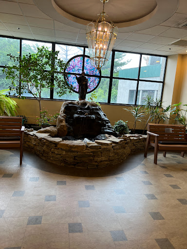 A serene indoor waiting area featuring a decorative fountain, comfortable seating, and abundant greenery.